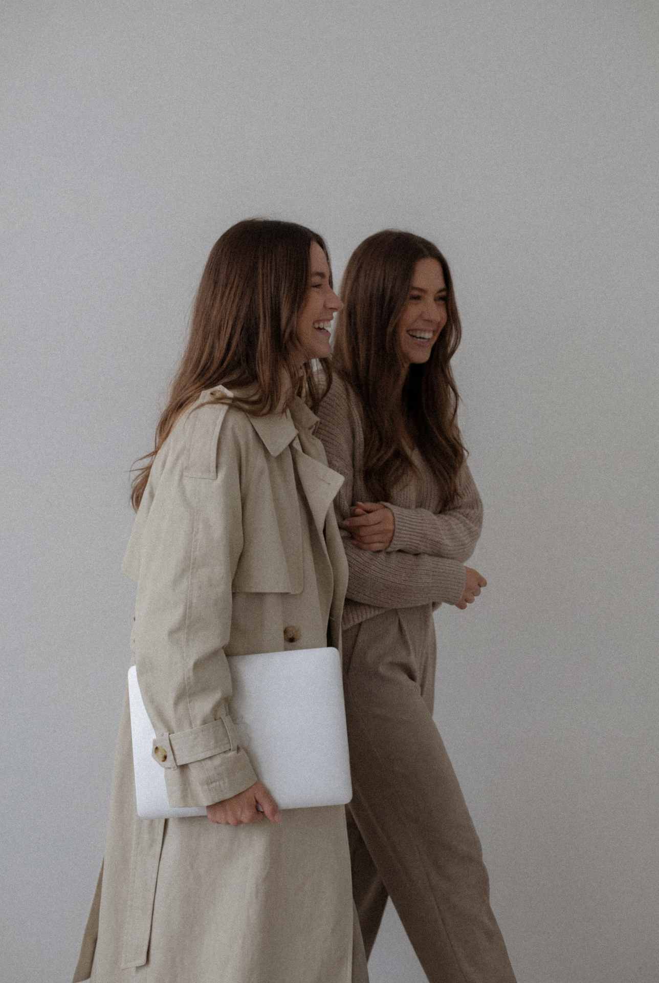 Two women in neutral tones laughing together